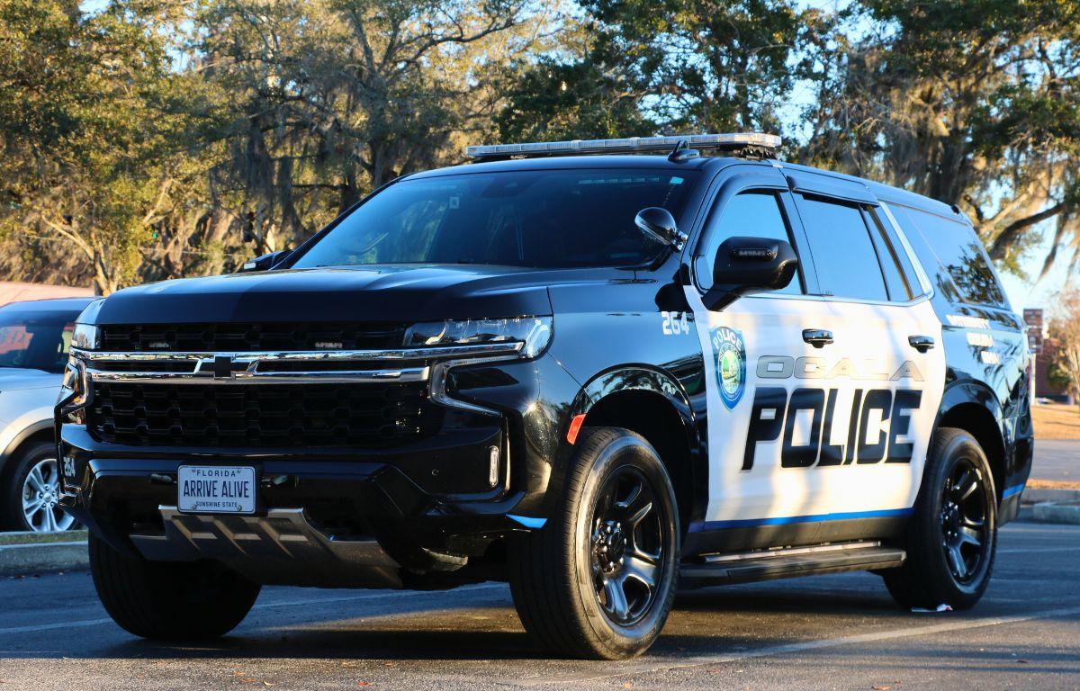 An Ocala Police car sits in a parking lot with the sun casting harsh shadows and reflecting off of it. "Ocala Police" is written on the side with a City of Ocala police logo toward the front.