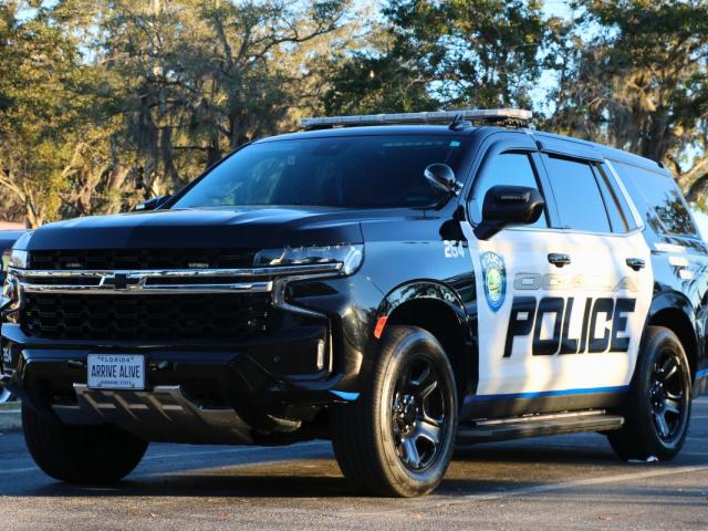 An Ocala Police car sits in a parking lot with the sun casting harsh shadows and reflecting off of it. "Ocala Police" is written on the side with a City of Ocala police logo toward the front.
