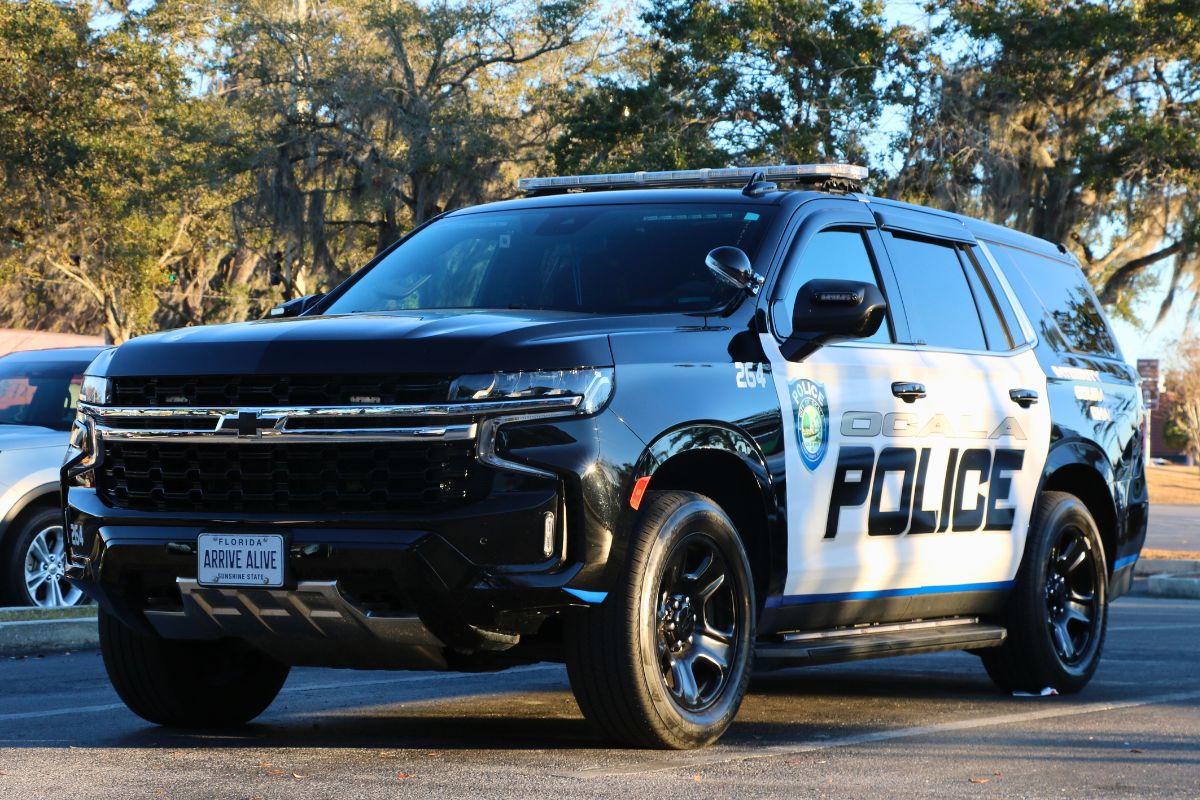 An Ocala Police car sits in a parking lot with the sun casting harsh shadows and reflecting off of it. "Ocala Police" is written on the side with a City of Ocala police logo toward the front.