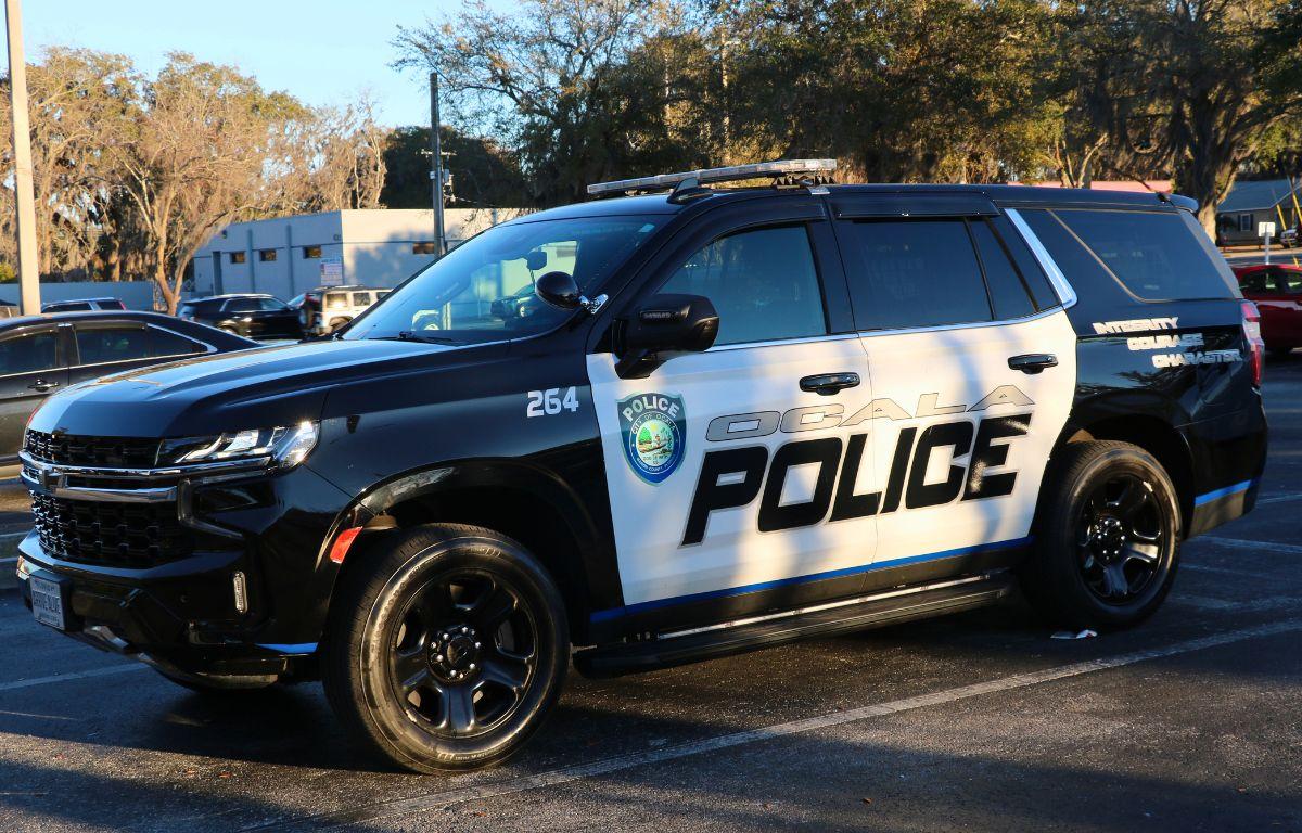 A black and white police car sits in a parking lot with silver and black text on the side reading, "Ocala Police," with a City of Ocala police logo next to it.