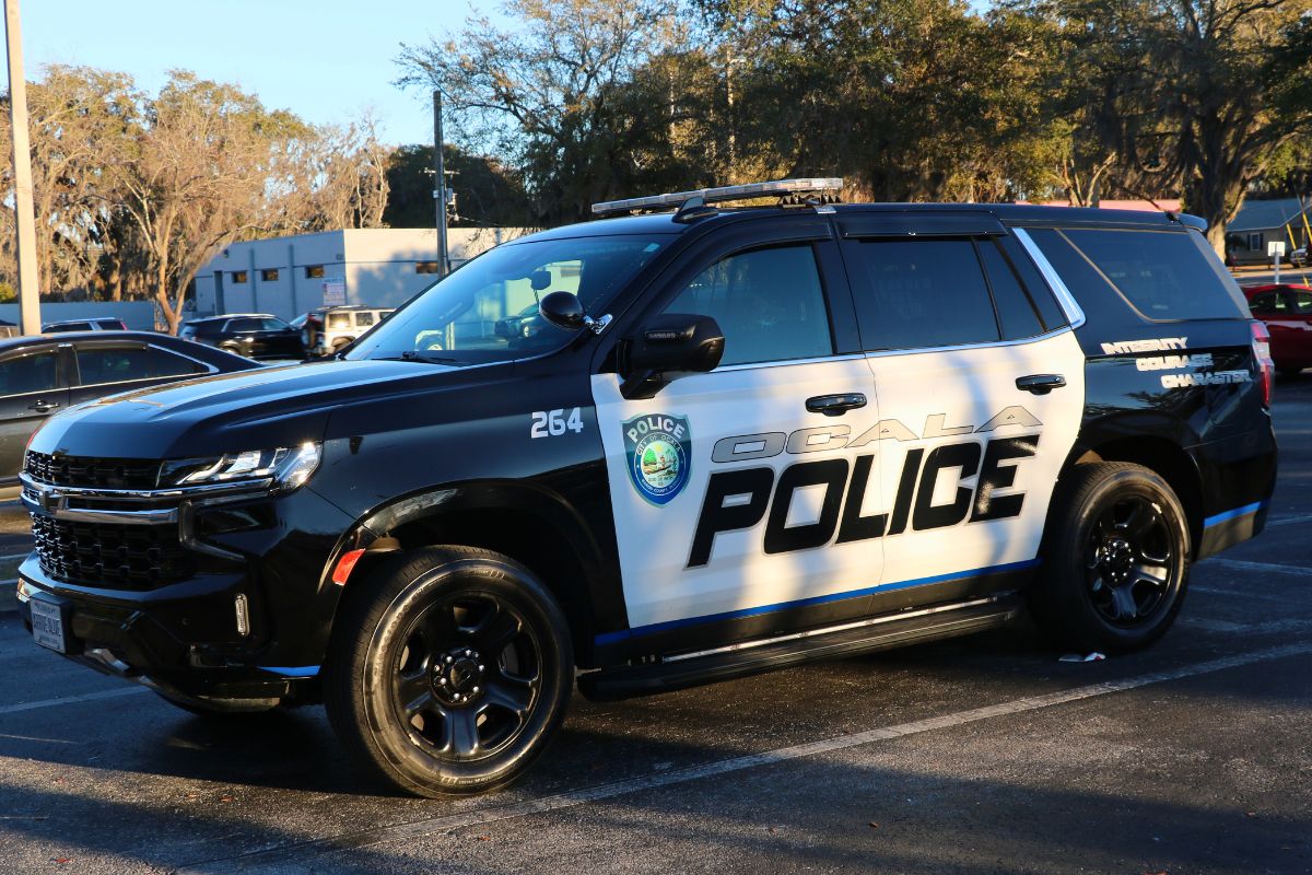 A black and white police car sits in a parking lot with silver and black text on the side reading, "Ocala Police," with a City of Ocala police logo next to it.