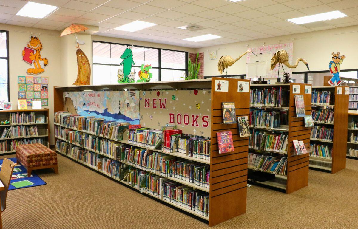 Five shelves are lined with books in a children's reading area. Stickers on the wall and characters on the shelves display fictional characters found in children's books and cartoons.