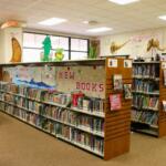 Five shelves are lined with books in a children's reading area. Stickers on the wall and characters on the shelves display fictional characters found in children's books and cartoons.