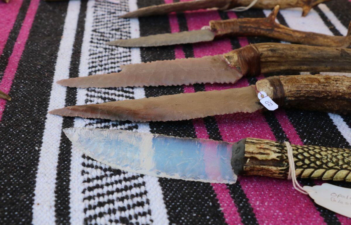 Multiple knives are displayed on a table with a pink, white and black tablecloth.
