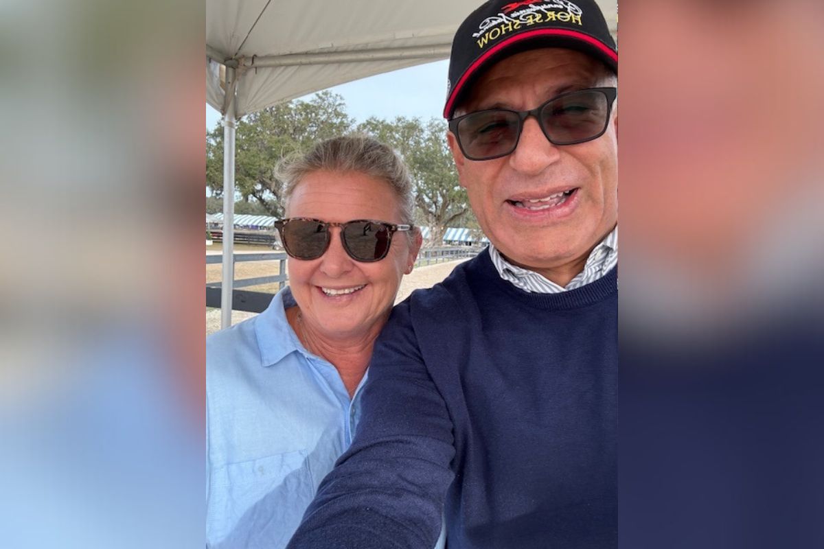 Woman and a man standing next to one another, with tents and horse stalls in the background. 