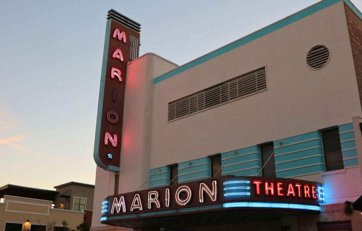 A large, beige, red and blue theatre with neon marquees read, "Marion Theatre."