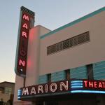 A large, beige, red and blue theatre with neon marquees read, "Marion Theatre."