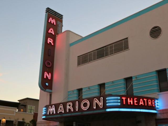 A large, beige, red and blue theatre with neon marquees read, "Marion Theatre."