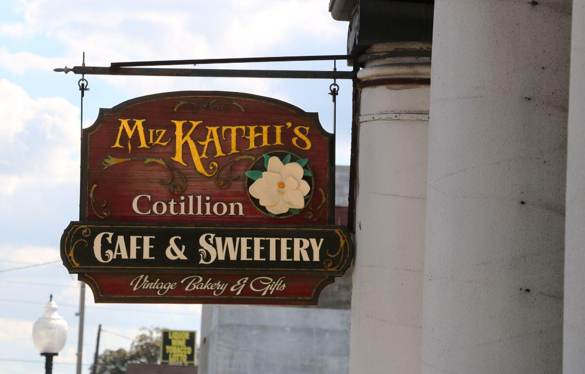 A sign hangs from a pillar with a vintage look reading, "Miz Kathi's Cotillion Cafe & Sweetery. Vintage Bakery & Gifts."