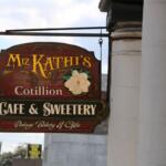 A sign hangs from a pillar with a vintage look reading, "Miz Kathi's Cotillion Cafe & Sweetery. Vintage Bakery & Gifts."