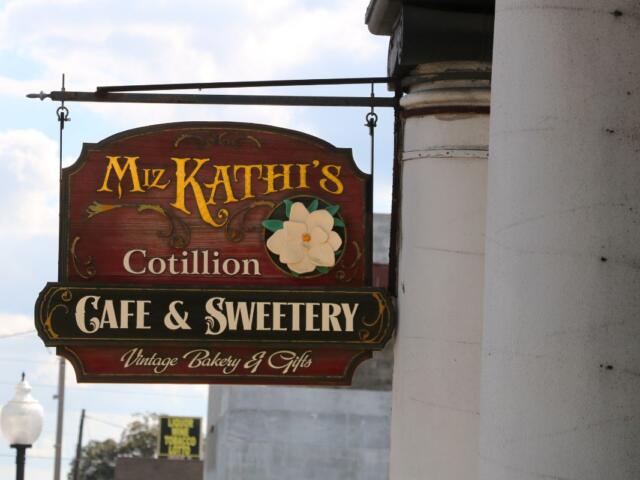A sign hangs from a pillar with a vintage look reading, "Miz Kathi's Cotillion Cafe & Sweetery. Vintage Bakery & Gifts."