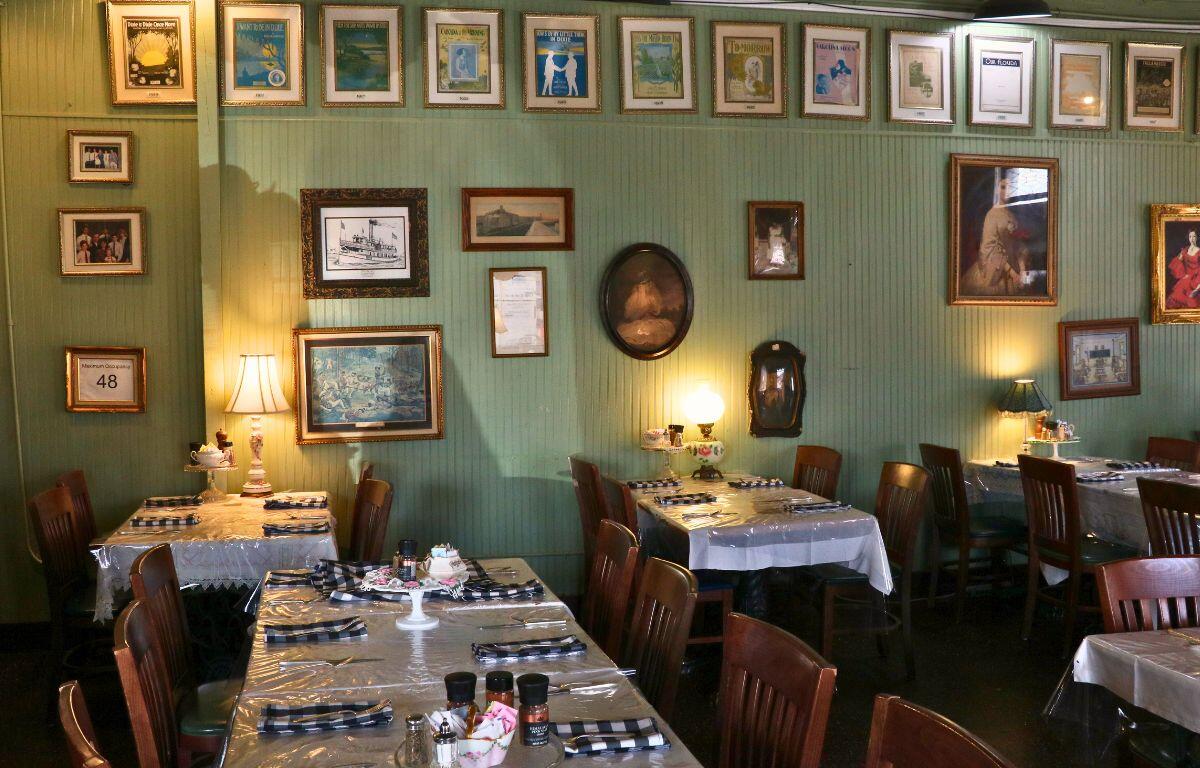 A restaurant with vintage decorations features tables scattered around the room with pictures of painted women, ships and Dixie advertisement from the early 1900s.