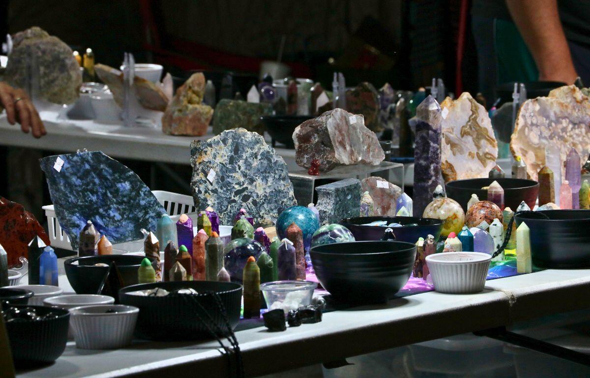 Two white tables feature a variety of crystals in different shapes and sizes on display with bowls featuring smaller ones.