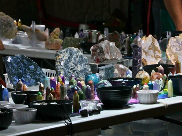 Two white tables feature a variety of crystals in different shapes and sizes on display with bowls featuring smaller ones.