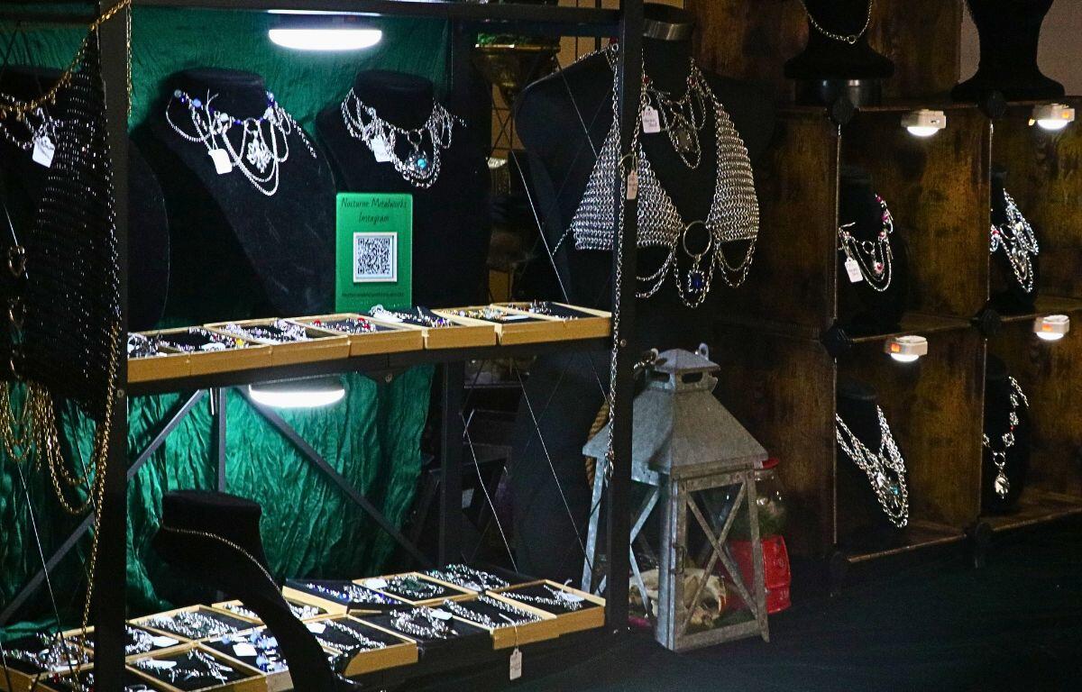 Metal jewelry is lined on shelves with small light fixtures on them. A lantern sits in the middle of the shelves.