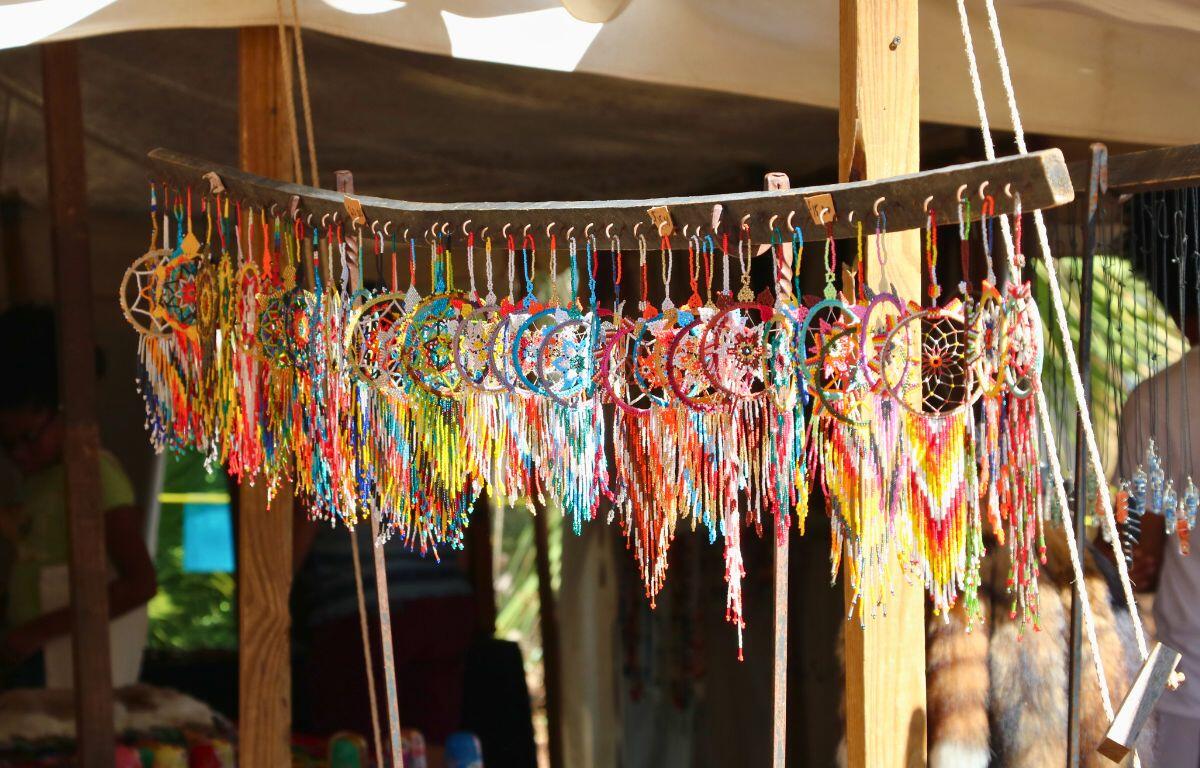 Miniature dream catchers are hung on a wooden figure in front of a canopied vendor at a market.