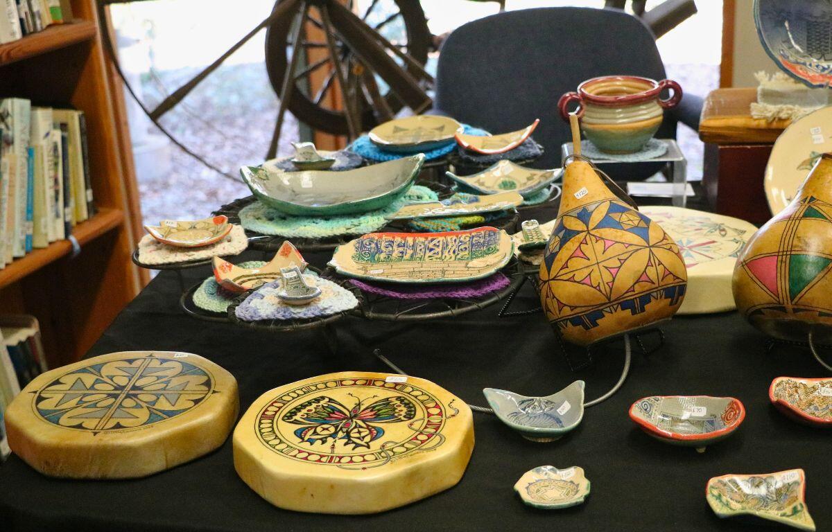 Mutiple hand-painted itemsare displayed on a table, including pottery and thunder drums.
