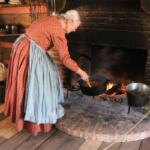 A woman in 1800s-themed attire stirs stew over a fire.
