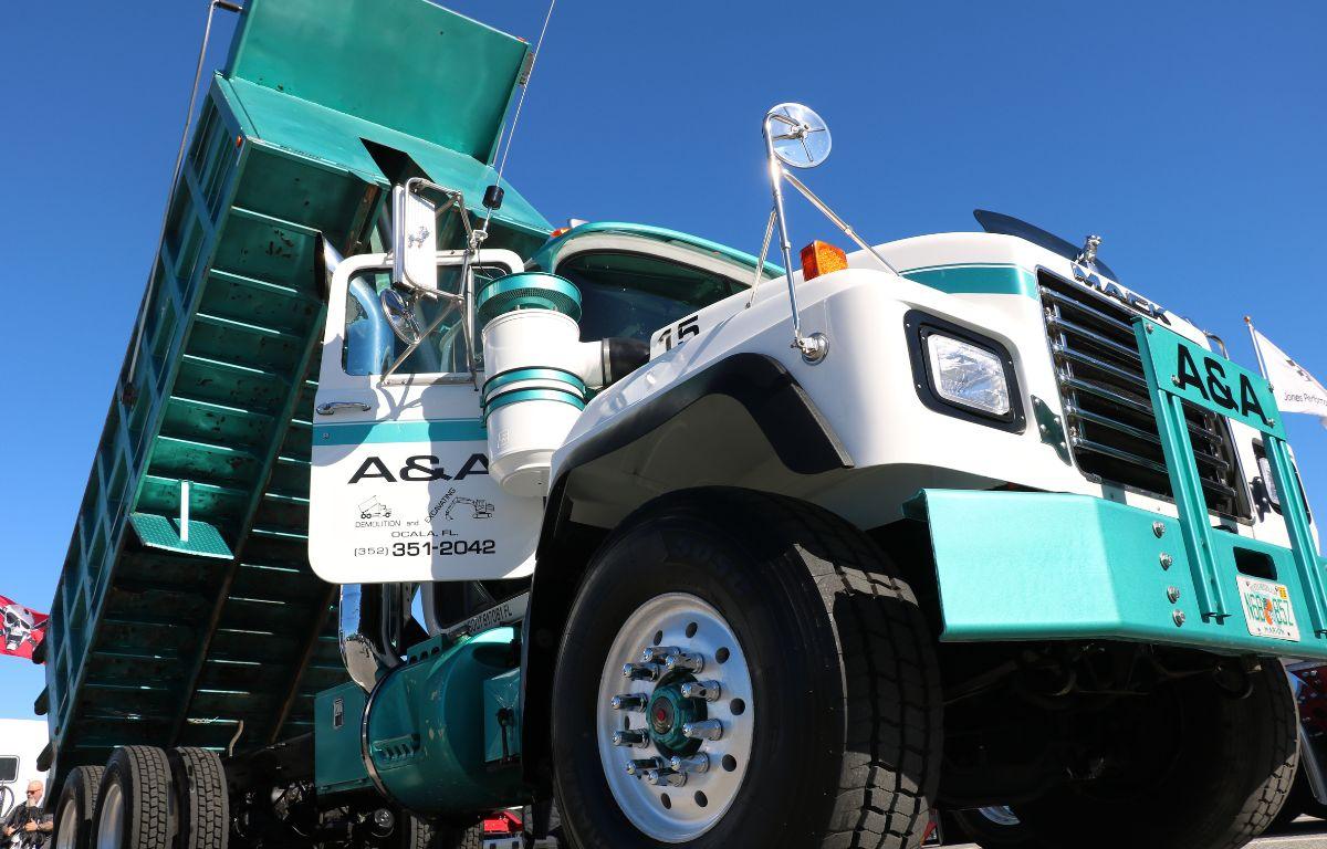 A large green and white truck has a container on the back, lifted up in a dump position.