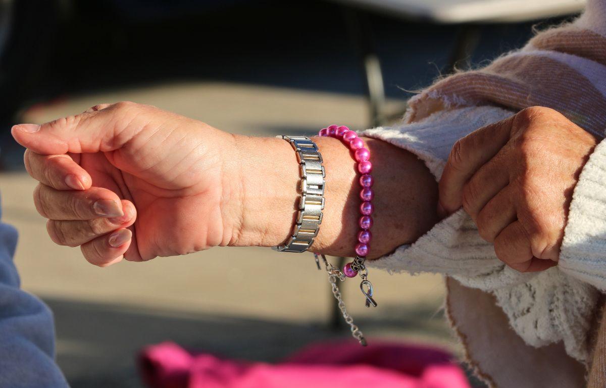 A woman shows a pink and silver bracelet on her wrist, pulling her sleeve back.