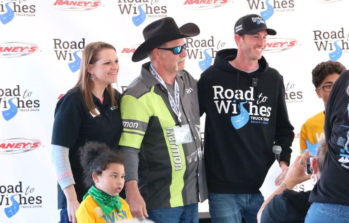A group of people stand together for a photo in front of a back drop that reads, "Road to Wishes Truck Show" and "Raney's."