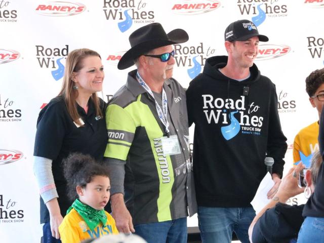 A group of people stand together for a photo in front of a back drop that reads, "Road to Wishes Truck Show" and "Raney's."