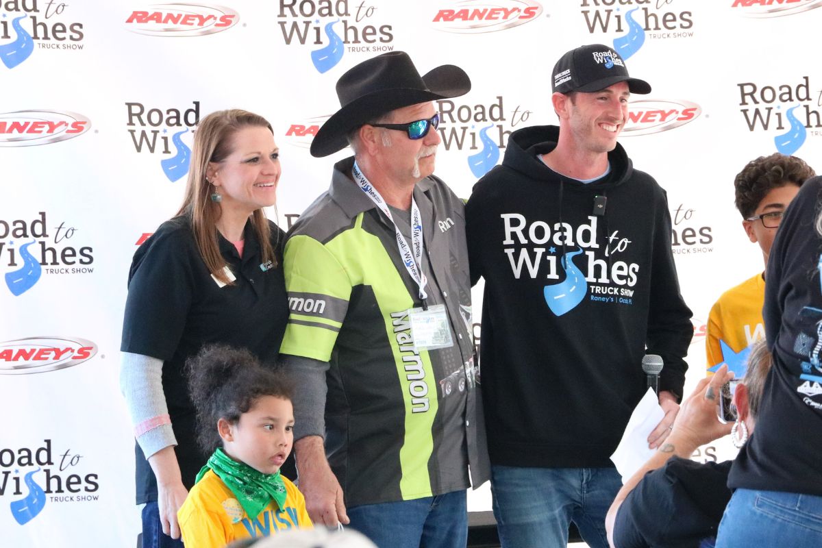 A group of people stand together for a photo in front of a back drop that reads, "Road to Wishes Truck Show" and "Raney's."