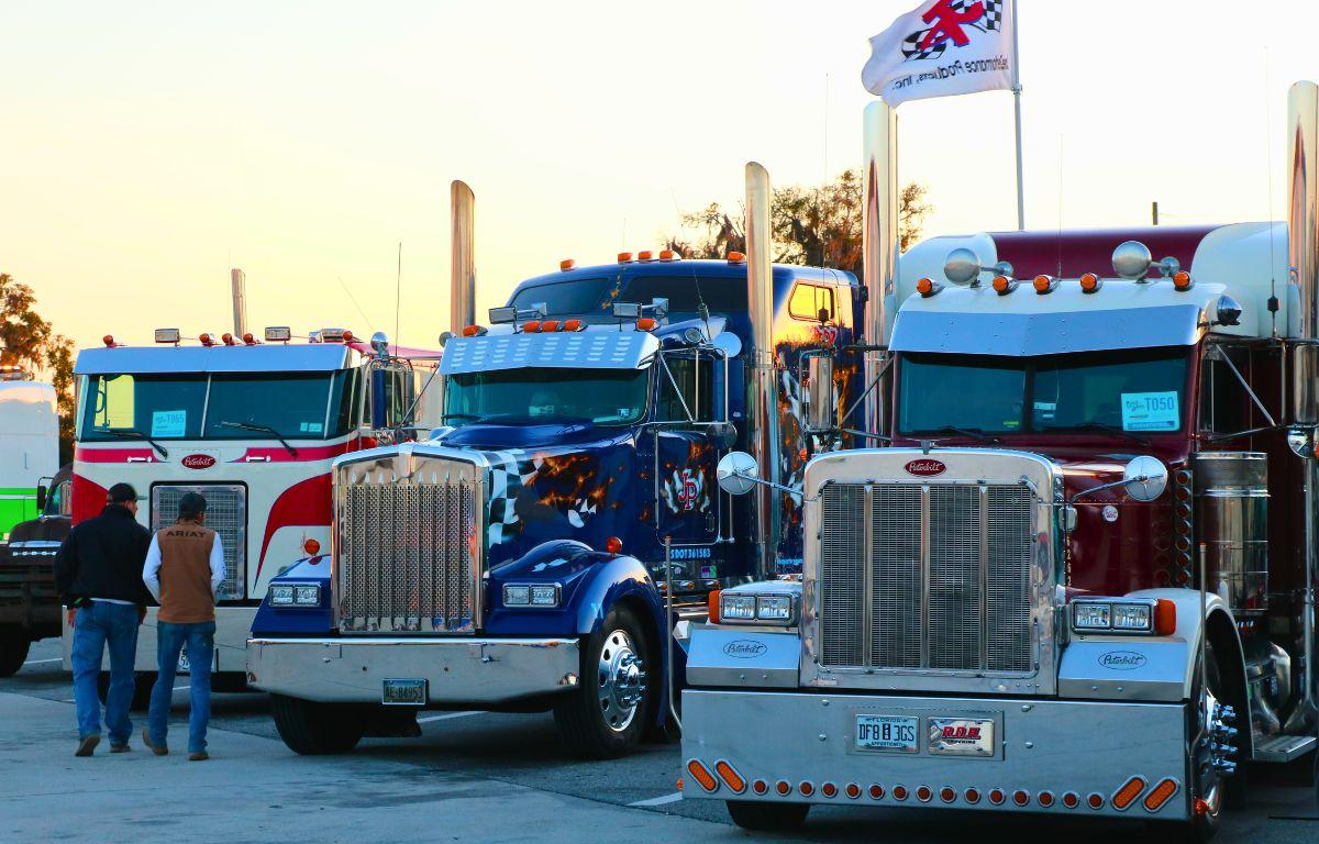 Trucks are lined up in a parking lot while people walk by, looking at them.
