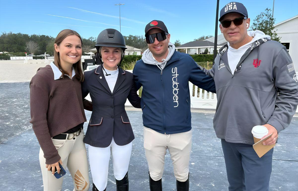 Two women and two men stand on a mat, in front of plastic barricades with structures in the background.