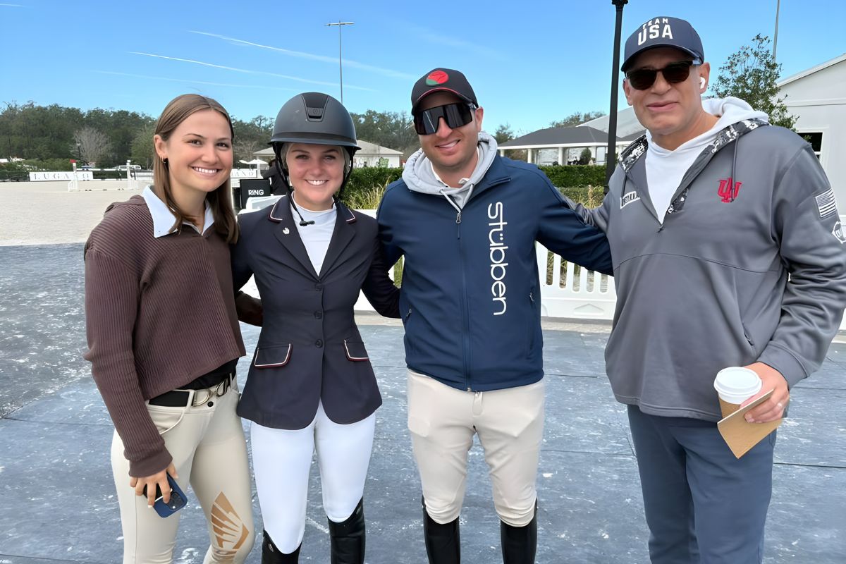 Two women and two men stand on a mat, in front of plastic barricades with structures in the background.