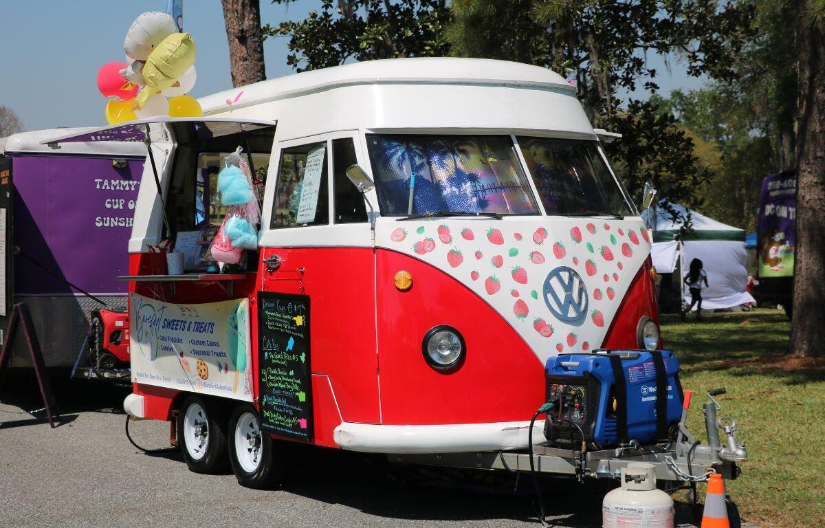 A white and red Volkswagen with strawberry designs on the front features an open window, acting as a food truck.