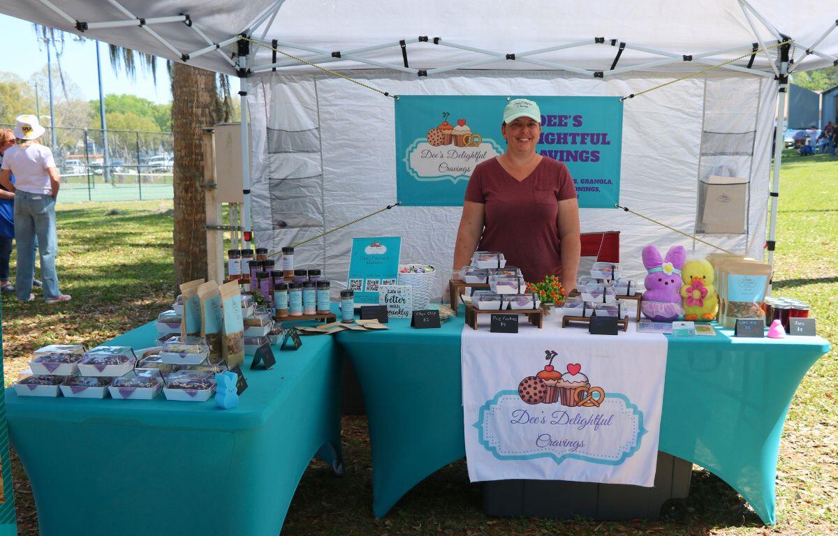 A woman stands behind a table under a canopy with advertising for Dee's Delightful Cravings.