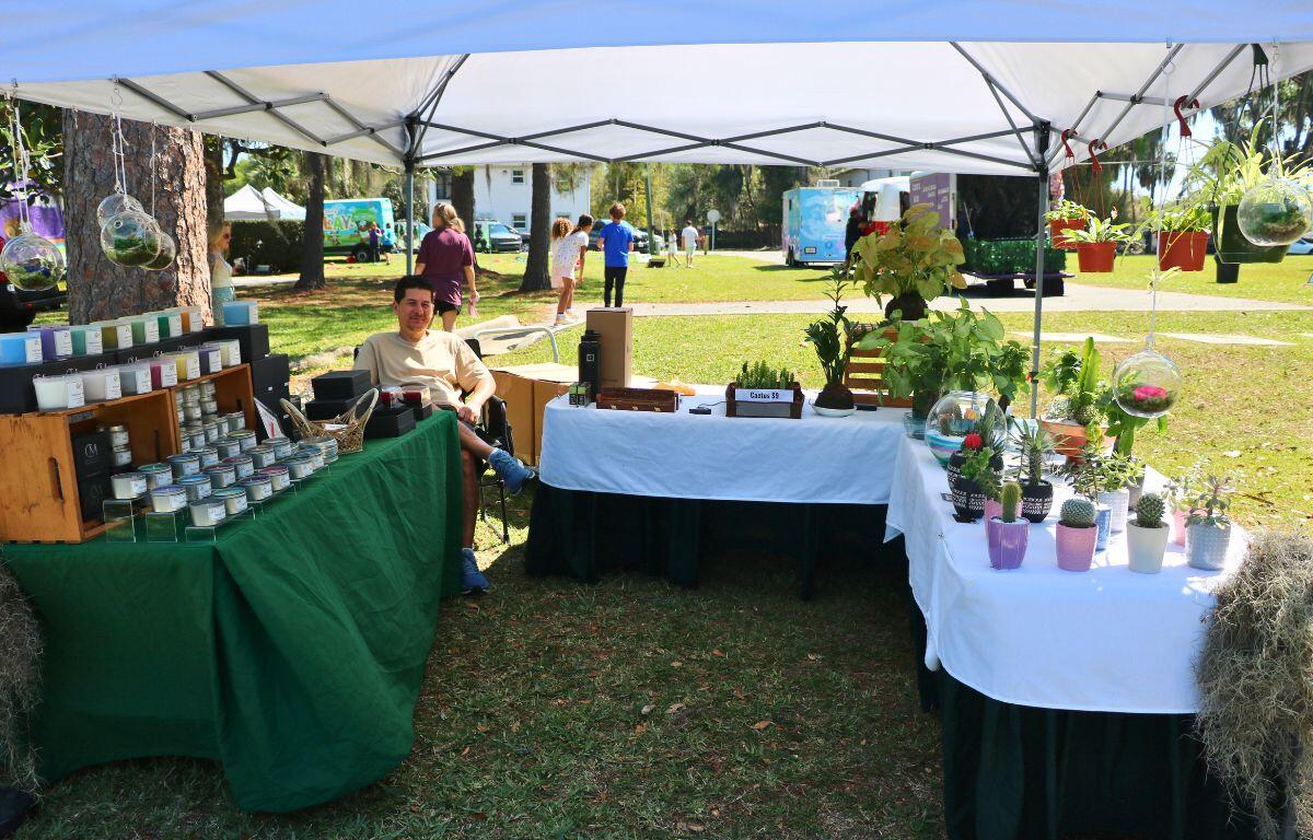 A man sits at the edge of tables with plants and candles scattered on them.