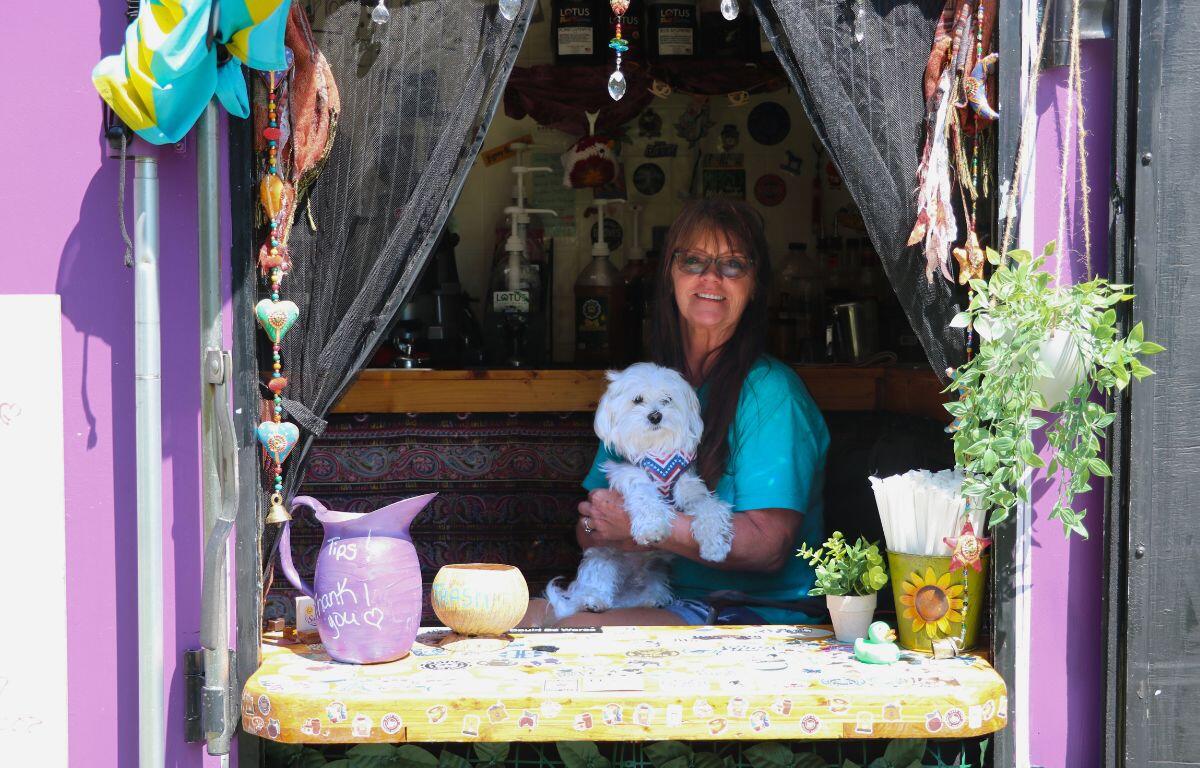 A woman and her dog sit in a food truck window with a variety of vibrant decorations around them.