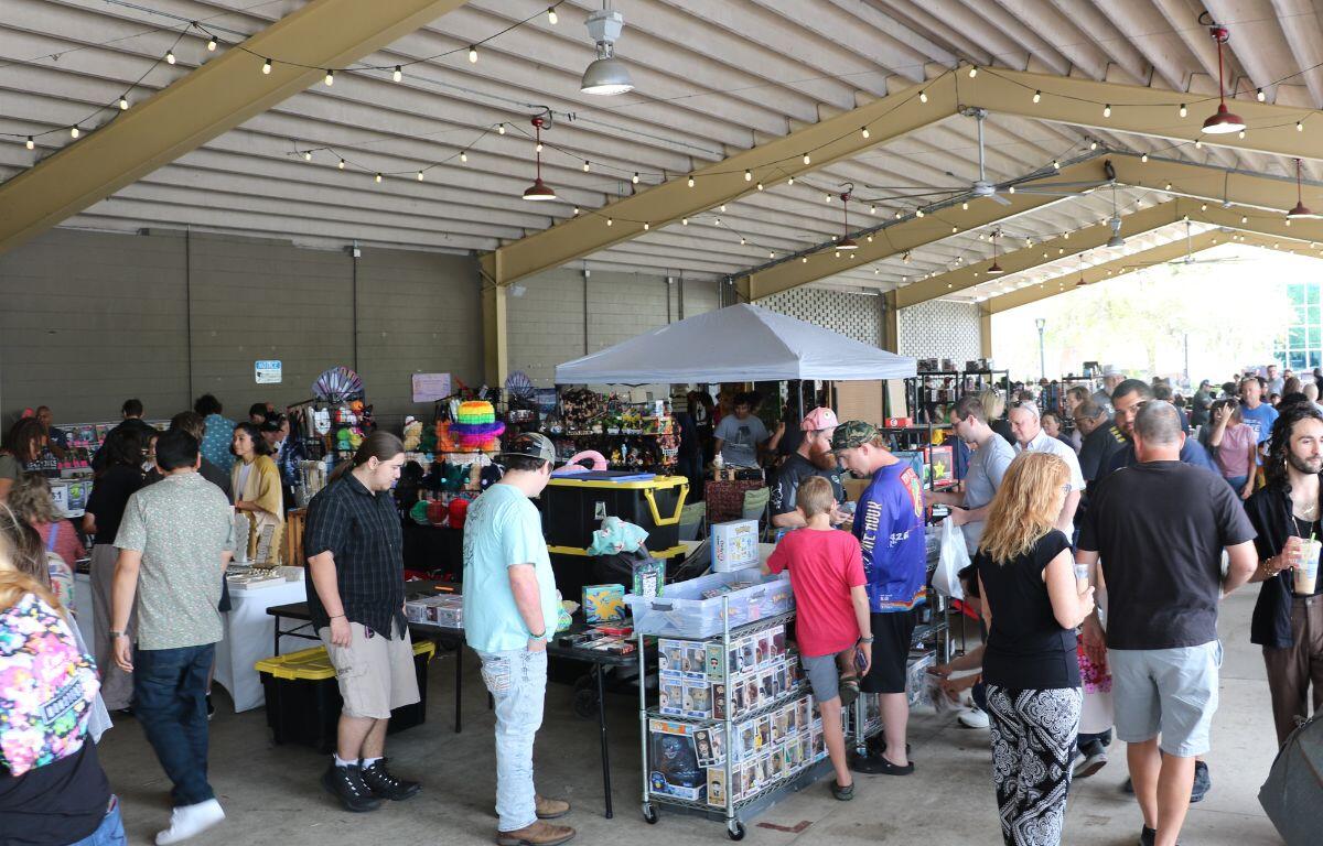 A crowd of people walk around a market, stopping to look at vendors.