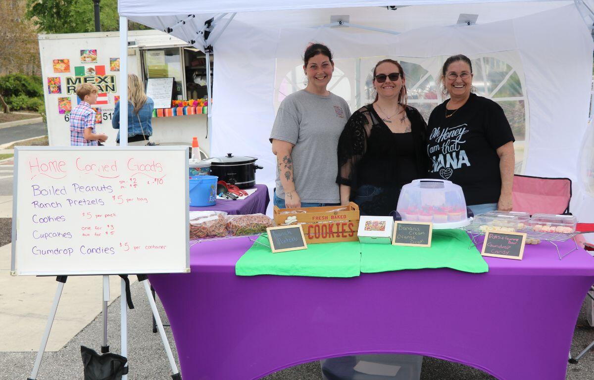 Three women stand behind a table of hand-baked goods.