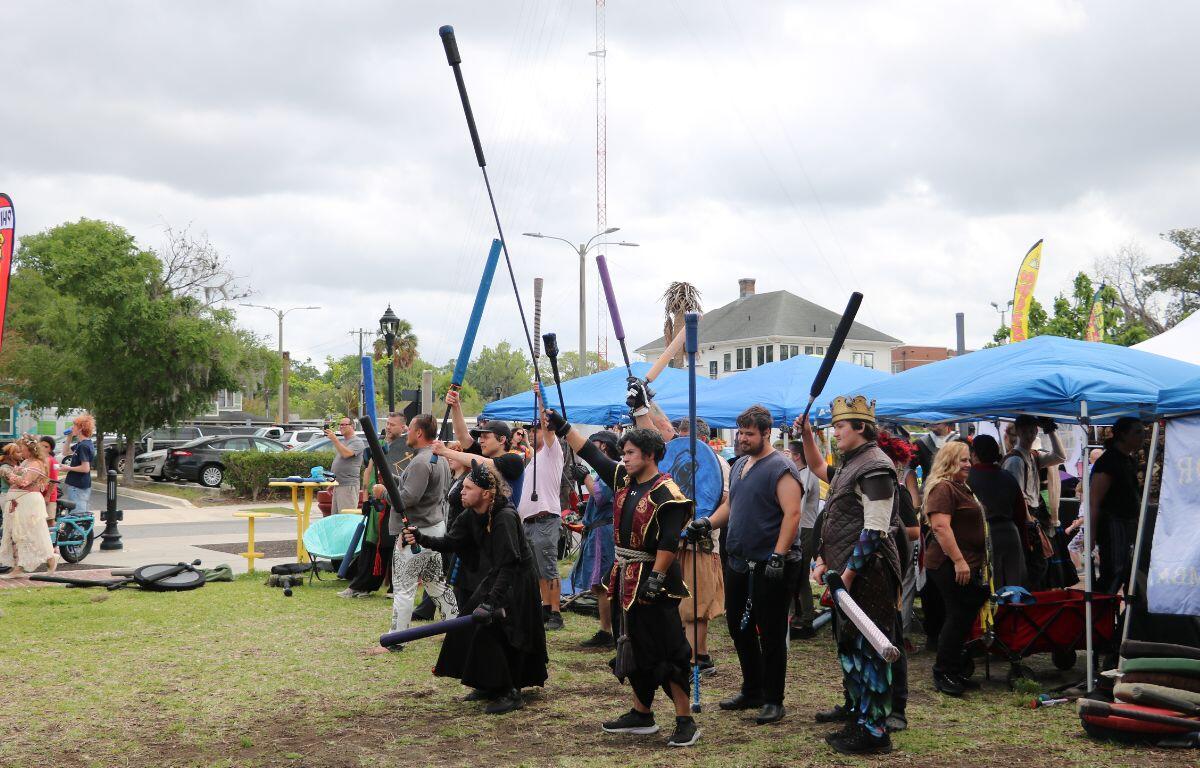 A crowd of people dressed in costume raise foam weapons, participating in live-action roleplay.