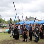A crowd of people dressed in costume raise foam weapons, participating in live-action roleplay.