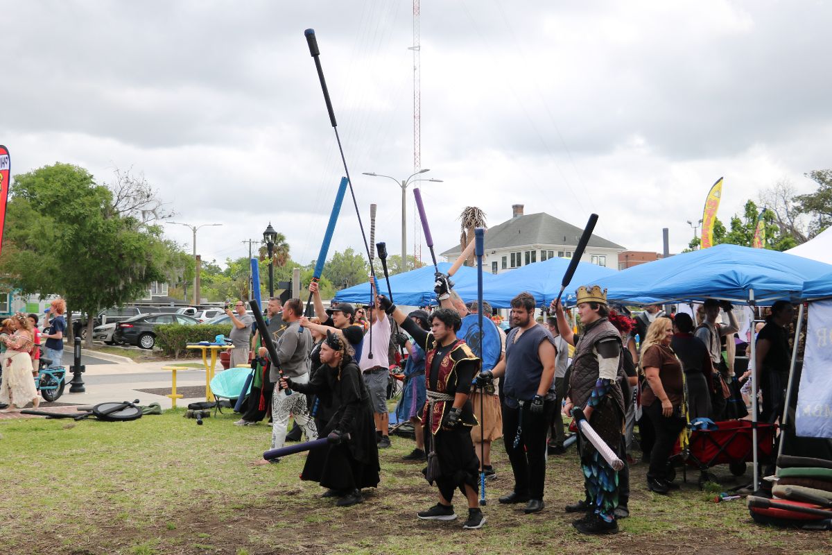 A crowd of people dressed in costume raise foam weapons, participating in live-action roleplay.