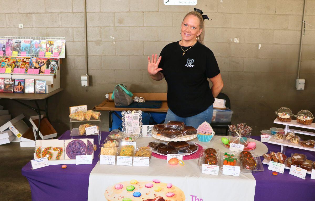 A woman stands behind a table with individually wrapped baked goods.