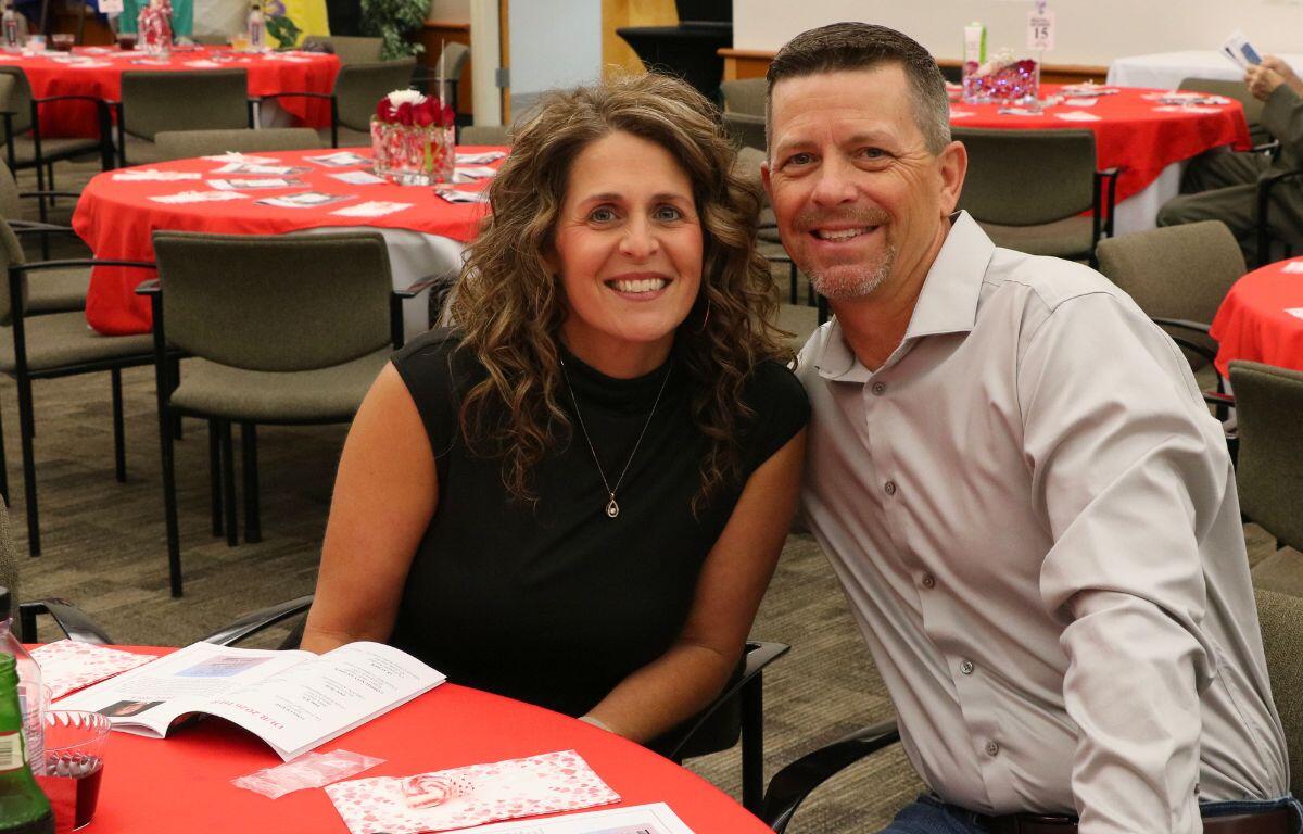 A couple sits together at a decorated table with open programs in front of them for a fashion show.