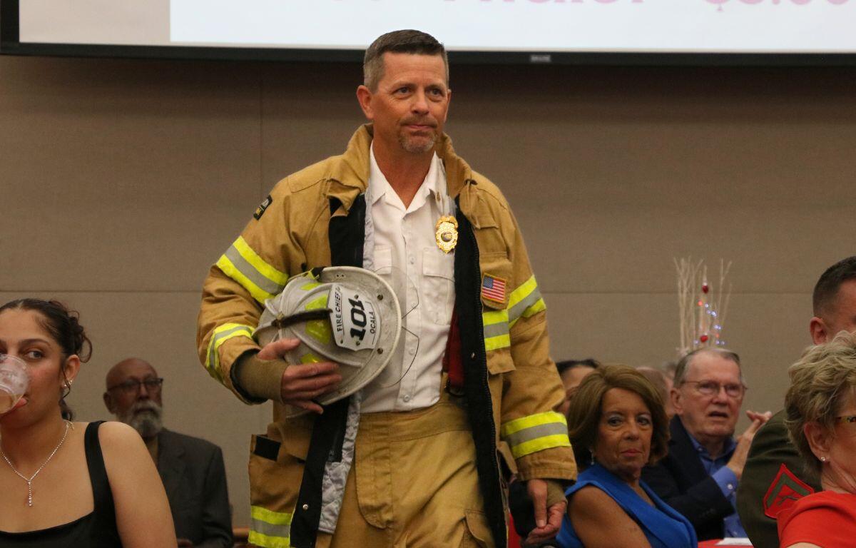 A man dressed in a firefighter uniform walks through a crowd of people with a stern look.