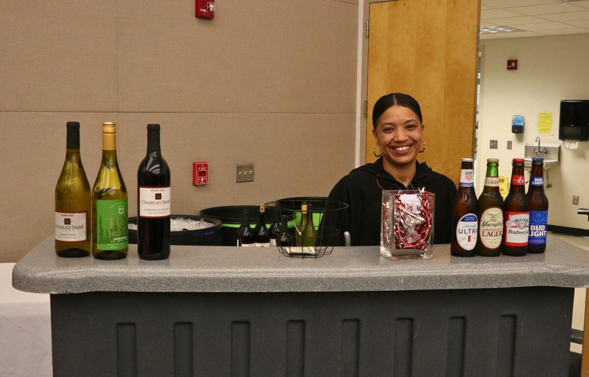 A woman stands behind a tall table with beer and white bottles on either side of it.