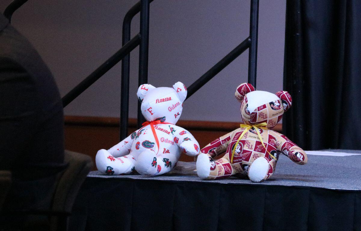 Florida Gators and Florida State University teddy bears sit next to each other on a stage.
