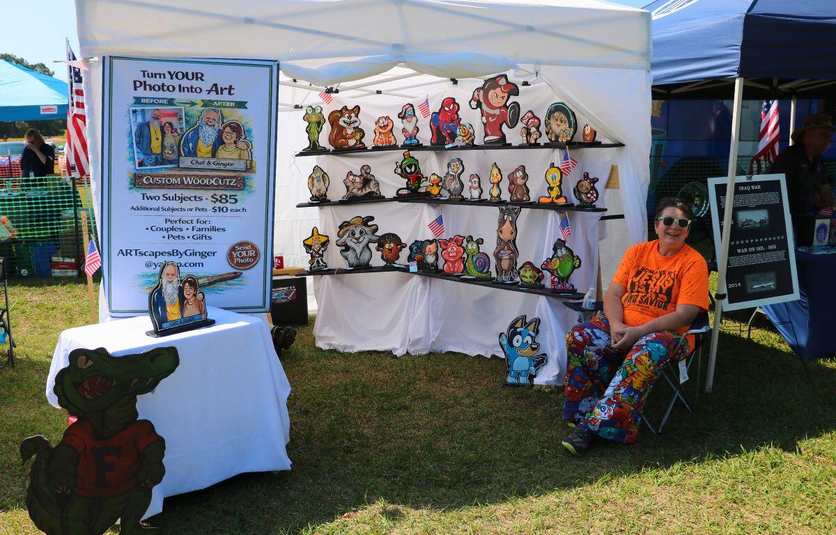 A woman sits in front of a large, white canopy with black shelves lining a wall inside. On the shelves are multiple wood carvings with small characters drawn on each one.