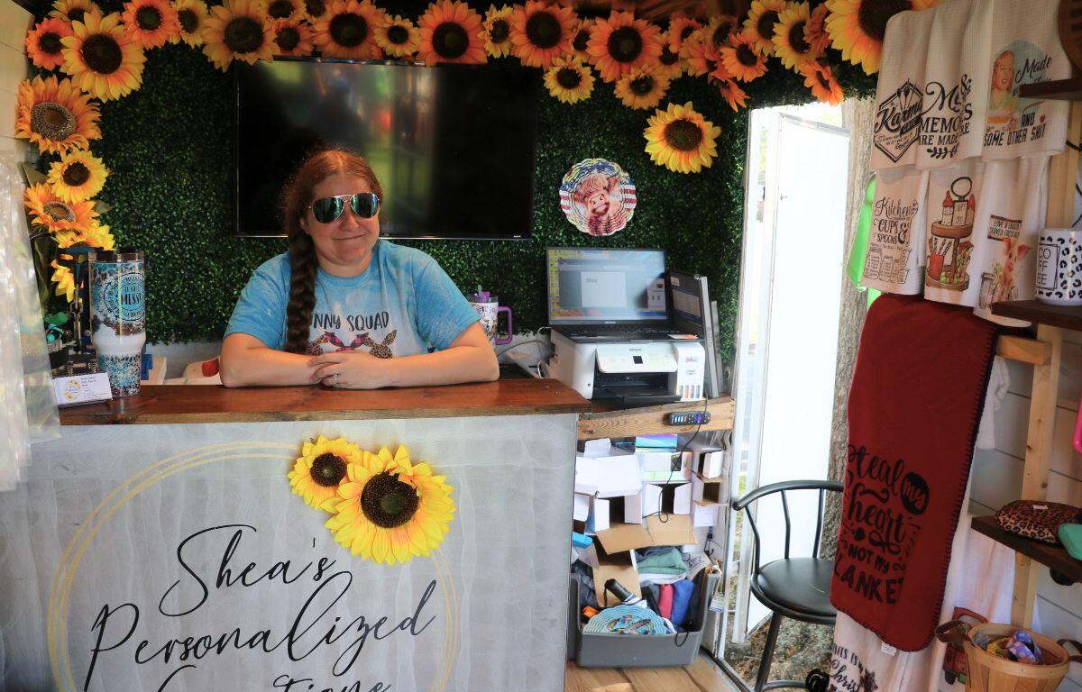 A woman stands behind a checkout counter decorated in sunflowers in a small shop with rags and decorative items for sale.