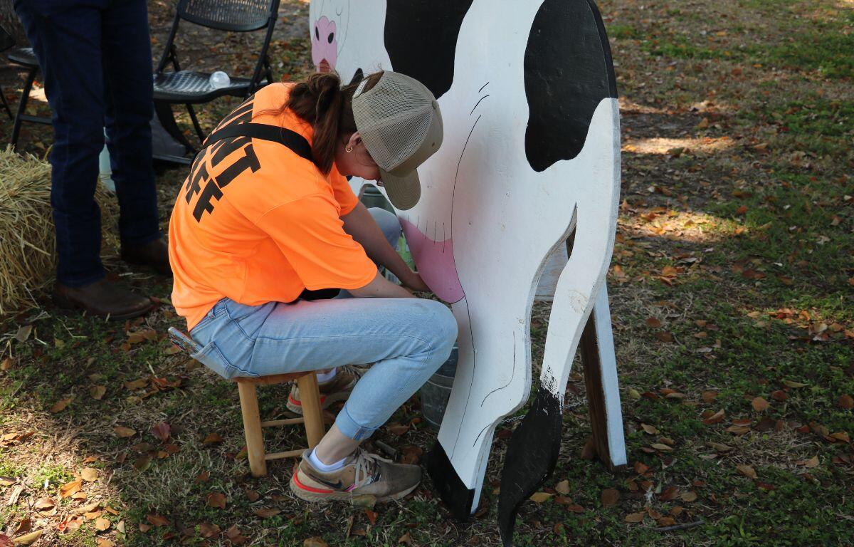 A woman demonstrates how to milk a cow with a wood cut out in the shape of a cow.