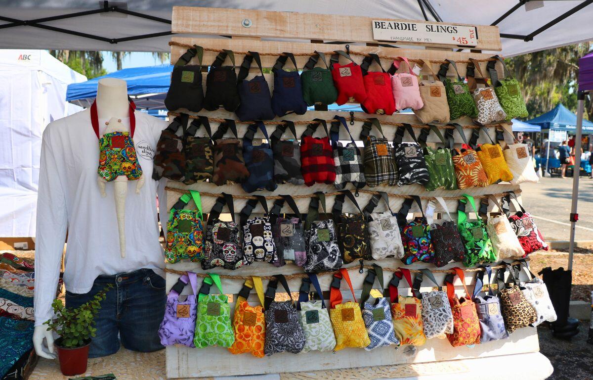 Small slings for carrying lizards are hung on a wooden wall. The sling are a variety of colors and patterns.