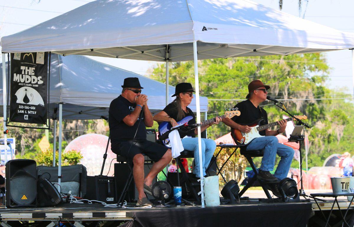 A band of two men and a woman play under a white canopy on a low stage.