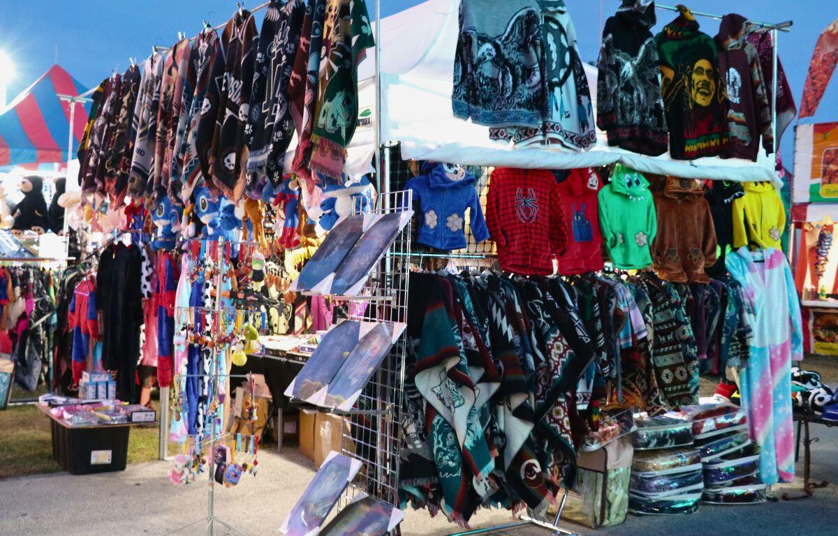 A vendor sells sweaters and t-shirts hanging on metal racks with sizes for adults and kids.